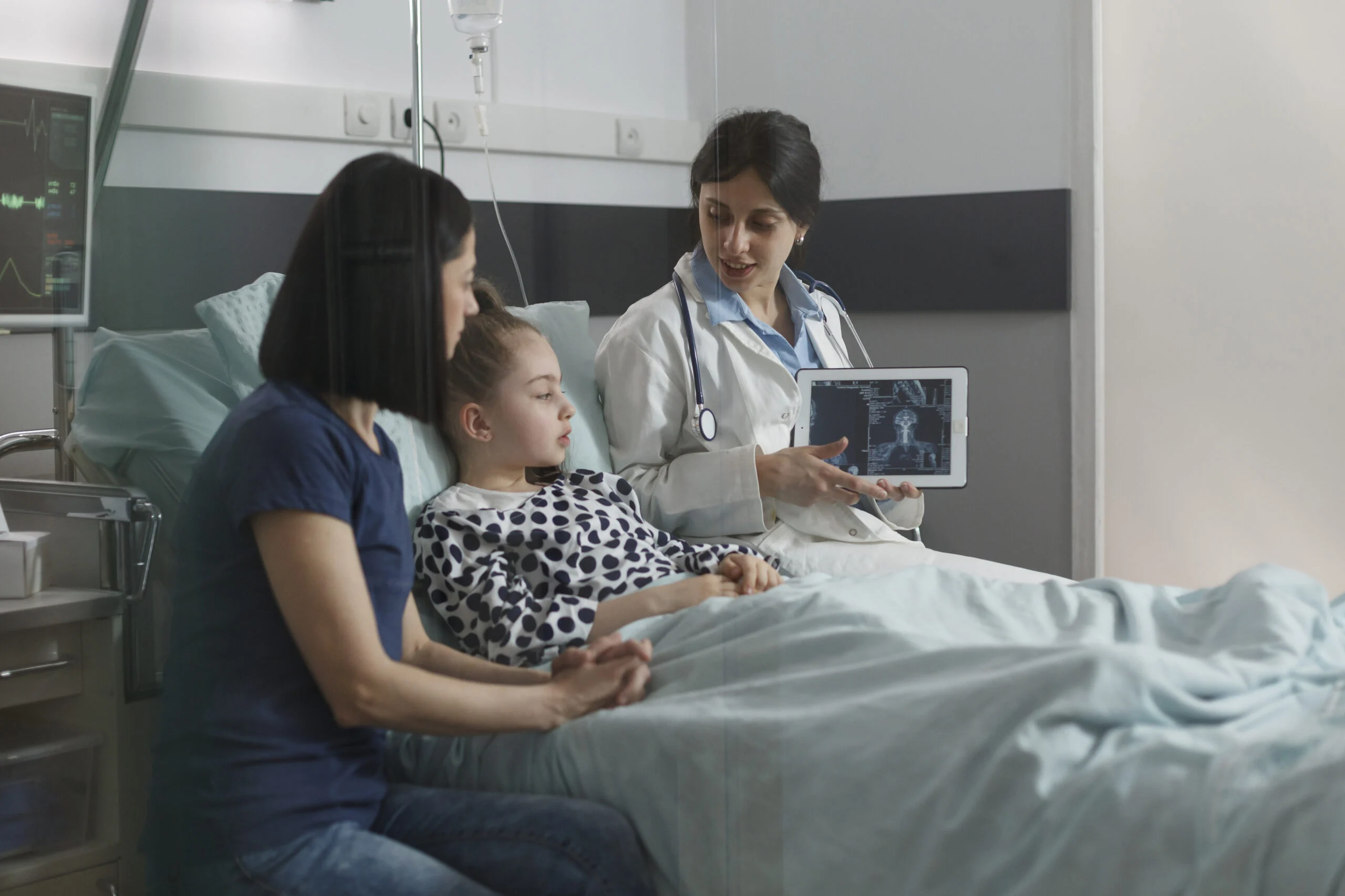 Dokter menunjukkan hasil pemindaian di tablet kepada anak sakit di ranjang rumah sakit, ditemani ibunya, suasana tenang.